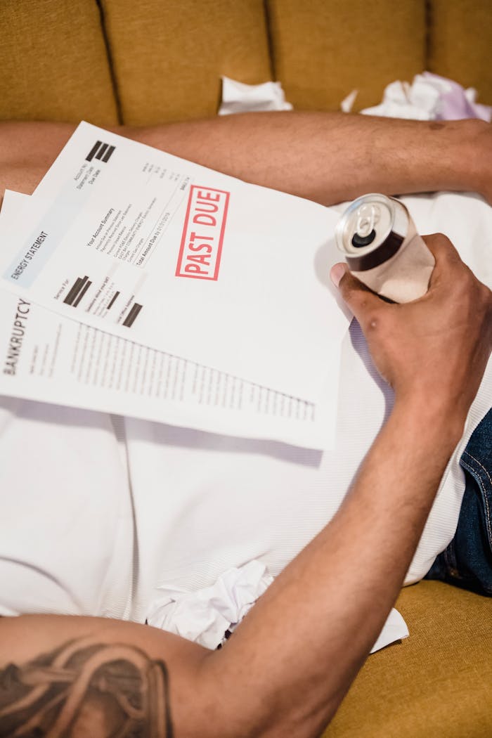 Close up of a Man Lying Down under Unpaid Bills Holding a Bear Can